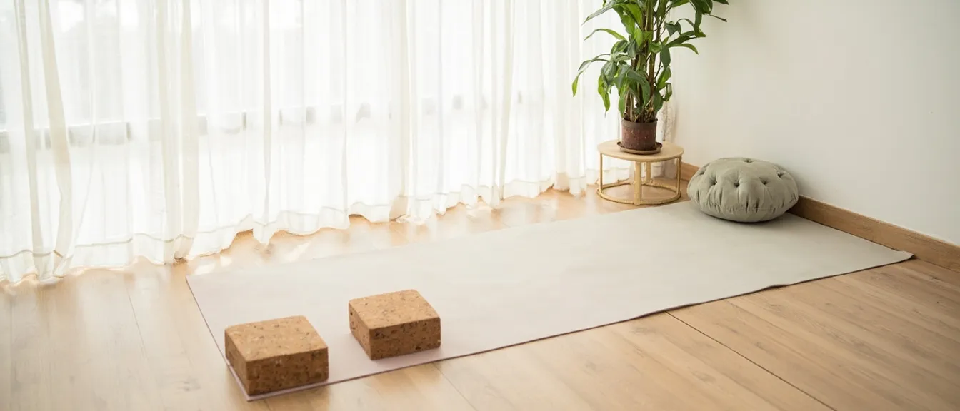 A calm apartment corner set up for at-home yoga with a pastel mat, cork blocks, and a sage meditation cushion in morning light